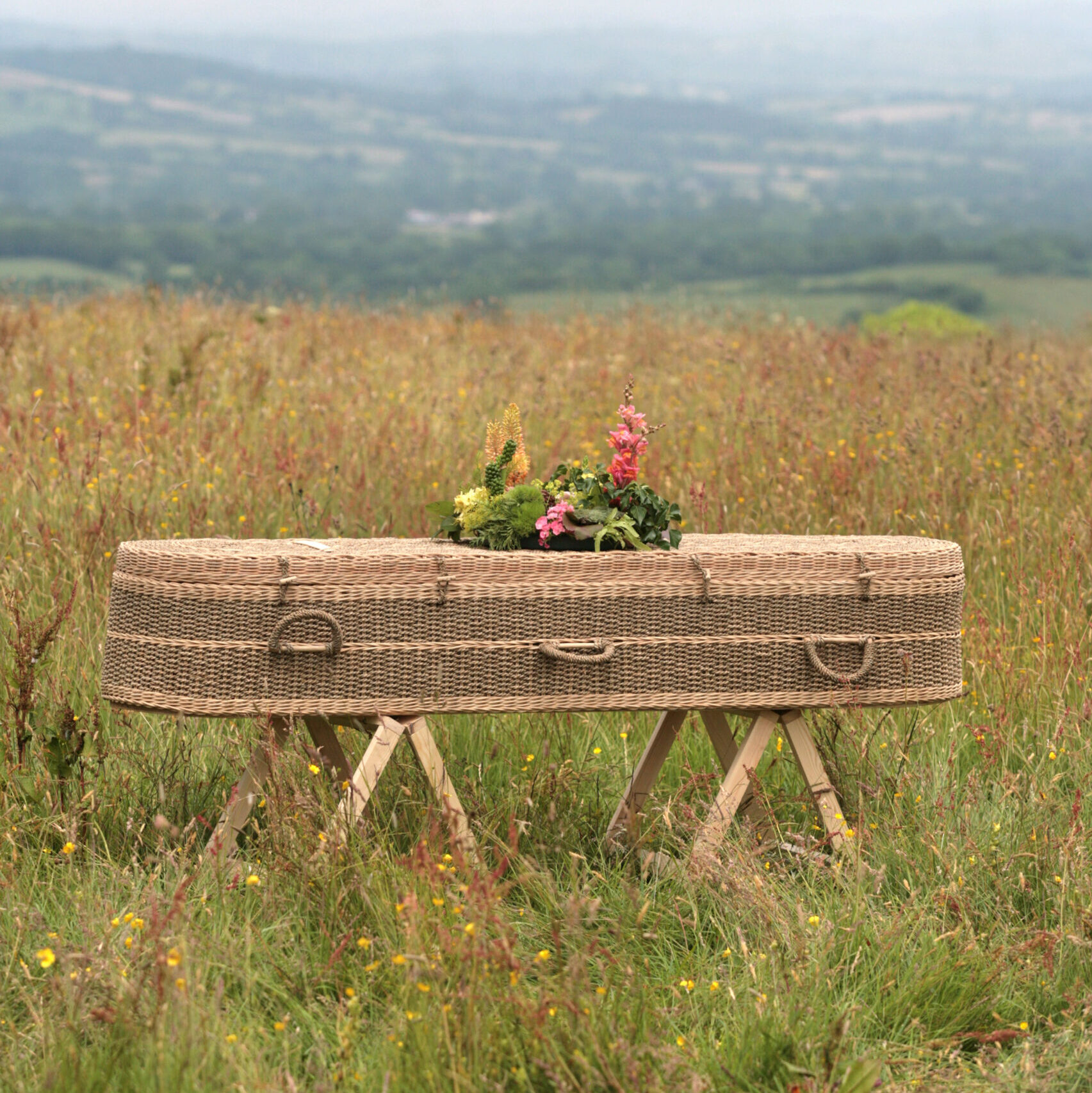 A wicker coffin with a bouquent on top in a wildflower meadow