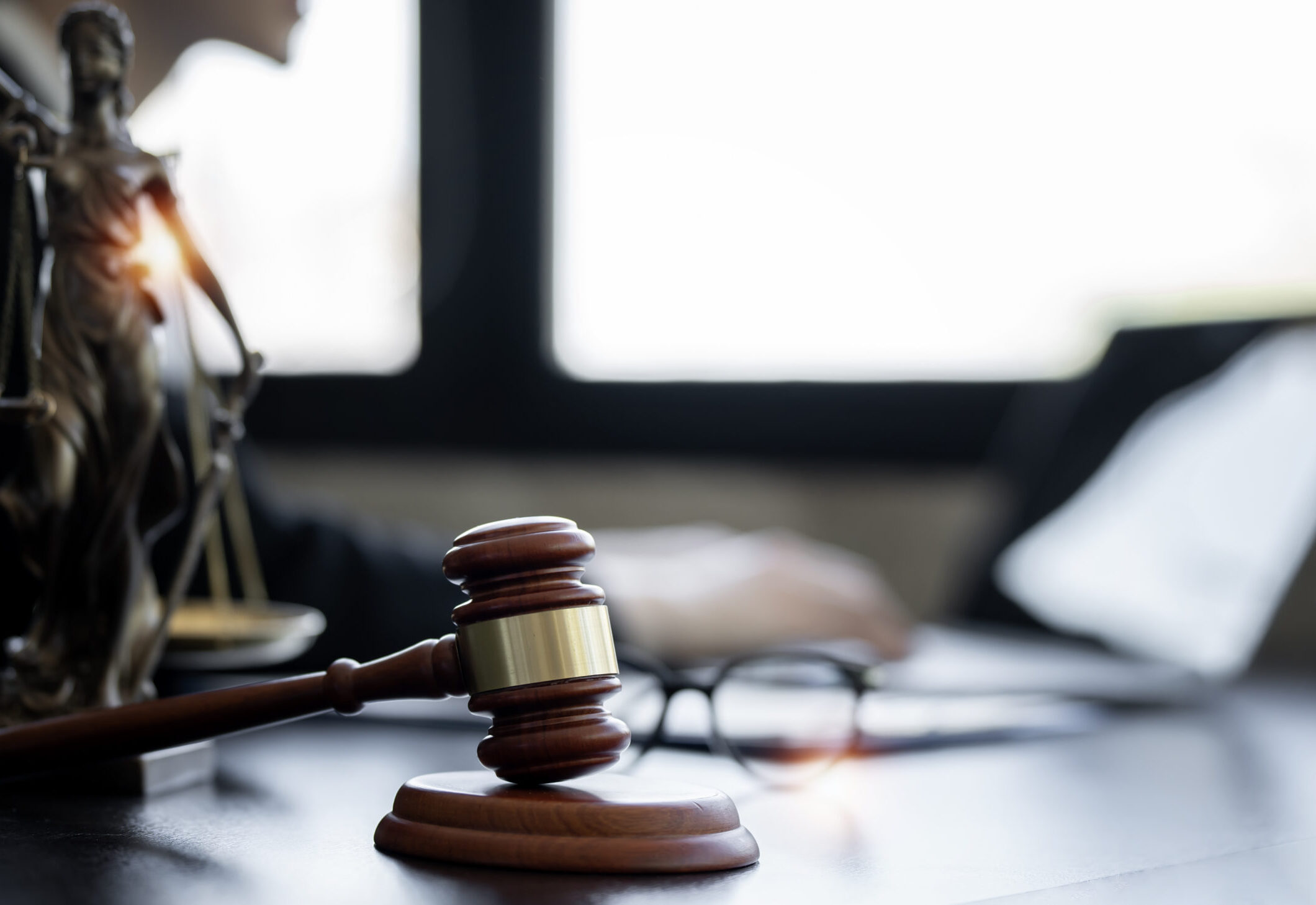 A gavel on a desk with glasses and a small figurine in the background