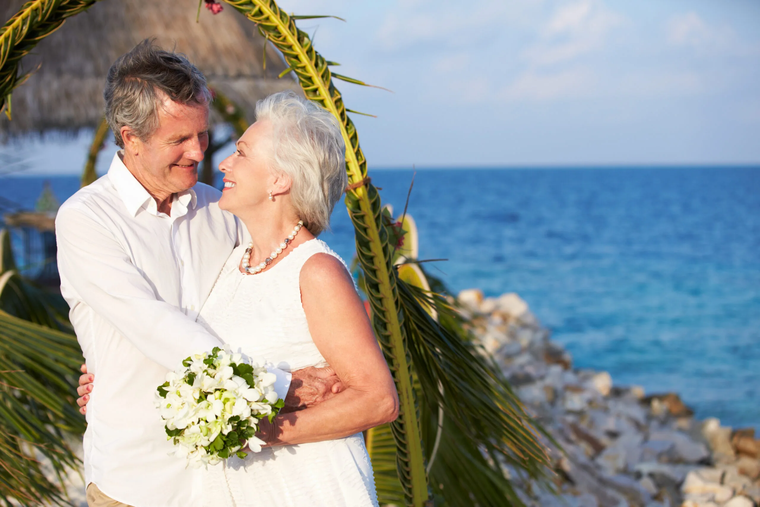 Senior Couple Getting Married In Beach Ceremony Looking At Each Other Smiling